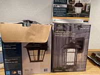 Photo showing two boxed Altair Lighting LED outdoor lanterns and one partially opened box of 10 solar pathway lights by Yards & Beyond.