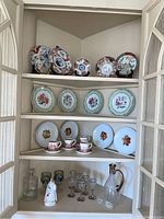 Upper china cabinet showing decorative plates on the top three shelves and glassware on the bottom shelf