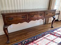 Sideboard showing full front view, wood finish, three drawer fronts and Queen Anne style legs.