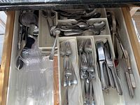 Drawer with dividers holding assorted stainless steel forks, knives, spoons, plastic utensils, and kitchen tools