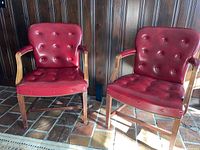 Two red leather library chairs with button-tufted backs and seats, wooden arms and legs, nailhead trim along edges.
