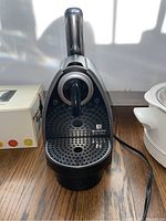 Nespresso Essenza coffee maker on floor, showing front side and drip tray.