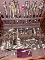Top down view of various spoons, forks, and serving utensils displayed within the wooden storage case.