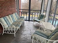 Patio furniture set including sofa, two chairs, and glass top coffee table on screened porch with stone floor
