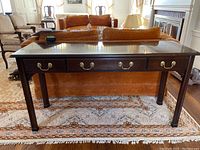 Full front view of dark wood sofa table with 3 drawers, brass handles, and showing slight blemishes on the surface.