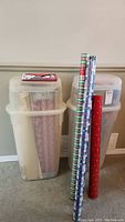 Two tall plastic storage totes stacked containing Christmas wrapping paper rolls and other wrapping materials.
