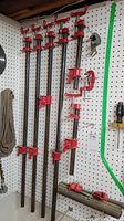 Five black steel pipe clamps with red cast iron heads mounted on pegboard