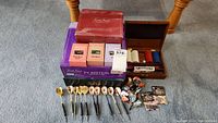Overview of boxed Trivial Pursuit games, darts laid out, wooden poker chip case with chips and cards