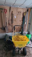 Wide shot showing spreader, extension cord, tarp, shovel, edger, hose sprayer and rake hanging on pegboard