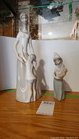Two Lladro figurines together on a wooden surface, showing size comparison.