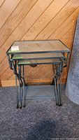 Photo showing the three nesting tables stacked together, highlighting metal frames and glass tops.