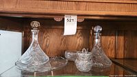 Two pinwheel crystal decanters, sugar bowl, serving platter, and trinket dish on a shelf.