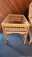 Front view of rattan side table showing rattan frame and glass top.