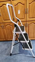 Side view of the white metal three-step folding step stool showing black steps and handlebar