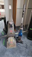 Bissell upright vacuum and ProHeat PowerSteamer side by side on carpeted floor with cords laid out, showing general lot items and condition.