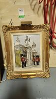 Full view of the framed vintage painting showing British royal guards at an ornate gate with attached art light above the frame.