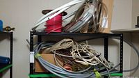 Wide shot of shelving unit filled with various coils of tubing and wiring, showing multiple spools and lengths of material.