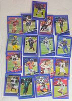 Top-down view of 16 Donruss Press Proof Blue Football cards laid out on white fabric, featuring various players in colorful action poses and blue borders.