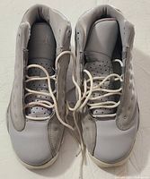 Top view of light grey Jordan 13 youth retro sneakers showing perforated tongue, laces, and toe box.