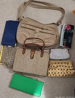 Beige shoulder bag, tan handbag, assorted clutches and fold-over wallets in various colors and patterns arranged on carpet.