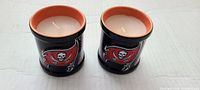 Pair of two black glass candles with Buccaneers skull and flag logo, white candles inside, measuring about 3.5 inches tall.