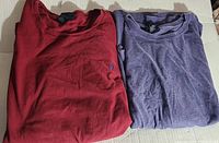 Both red and purple vintage Polo Ralph Lauren shirts folded on cardboard surface.