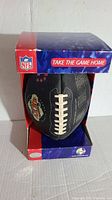 Photo of the limited edition black Super Bowl XXXV football in original red, white, and blue NFL branded box, showing football partially out of the box with laces visible.