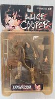 Front view of sealed Alice Cooper action figure in original packaging showing figure, snake accessory, microphone stand, cane, top hat, and extra head.