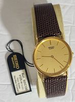 Front view of the gold-tone Seiko quartz watch with gold dial, hour markers, hands, and attached tag showing model number and price.