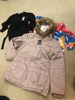 Lot of three clothing items: beige Cabin Parka with faux fur hood, black Aero hoodie, and colorful Revamped sweater top, laid flat on beige carpet.