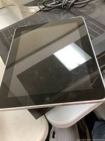 Front top view of black iPad with physical home button on a table, showing screen and bezel.