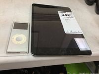 Apple iPad and Apple iPod side by side on a surface showing size comparison and condition.
