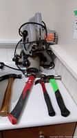 Photo of Black and Decker circular saw and three hammers on a white countertop.