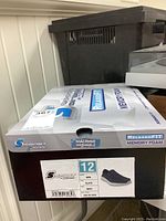 Photo of the original Skechers S Sport shoebox showing size 12, men's Claye navy runners with relaxed fit and memory foam.