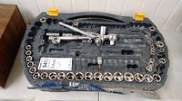 First photo showing an open molded plastic case with a nearly complete set of chrome sockets of various sizes arranged along the edges, and several ratchets and extensions placed in the center of the case.
