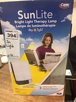 Box front showing brand Carex, product name SunLite Bright Light Therapy, image of woman using lamp, and branding Day Light.