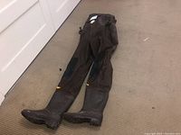 Full view of brown waders with attached boots laid out on carpet.