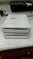 Two stacked white Nintendo Wii RVL-001 consoles, scuffed and scratched, without cables or controllers.