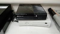 Two Xbox 360 consoles stacked, black one on top and white below, no cords or controllers visible.