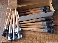 Box containing 12 wooden handled artist poster brushes with black bristles, new in packaging.