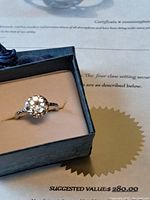 Ring with round blue topaz stone set in a four-claw sterling silver setting inside a black box on top of certificate showing suggested value.