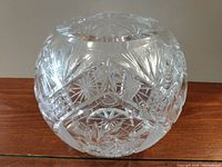 Round clear crystal vase with cut starburst and geometric patterns shown from side angle.
