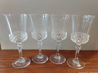 Four clear crystal wine glasses with faceted diamond-cut pattern around the lower bowl, slender stems, and circular bases, displayed on a wooden surface.