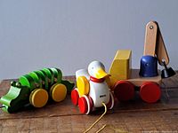 Green segmented wooden alligator with yellow wheels, white Brio duck with red wheels and yellow wings, and yellow wooden crane toy with red wheels and movable arm with magnet.
