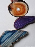 Three polished agate slices in orange-brown, purple, and blue colors on a white background.