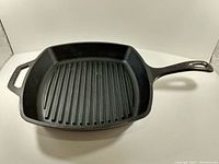Square cast iron grill pan with ribbed cooking surface, handles, and black finish.