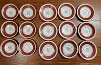 Fifteen Paragon bone china saucers laid out on wooden surface showing floral pattern with burgundy and gold trim.
