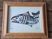 Full view of the indigenous salmon print framed in wood and behind glass, showing design and signatures.