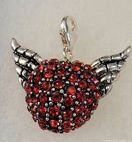 Close-up front view of the charm showing red crystals encrusted on a winged heart design with silver lobster clasp for attachment.