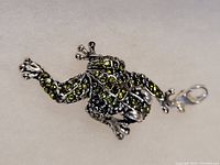 Front view of frog charm showing green stones and details on limbs and head.